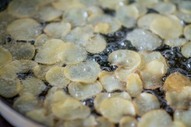 Tavada dilimlenmiş patatesler kızgın yağda kaynıyor.