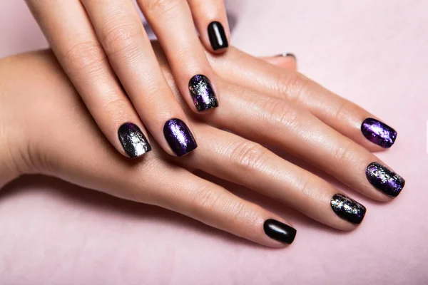 Closeup top view of two beautiful hands of woman with professional manicure, nails painted with black color and covered with glance top with glossy shine.