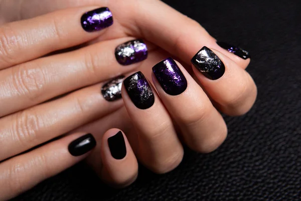 Closeup top view of two beautiful hands of woman with professional manicure, nails painted with black color and covered with glance top with glossy shine.