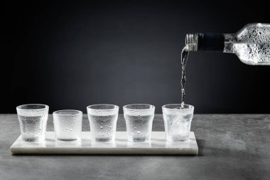Karanlık arka planda izole edilmiş shot bardağına soğuk votka dökülüyor. Seçici odak.