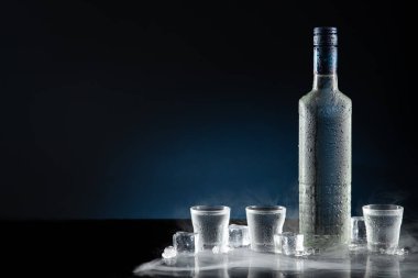 Buzlu votka şişesi shot bardakları ile koyu mavi arka planda fotokopi alanı ile.