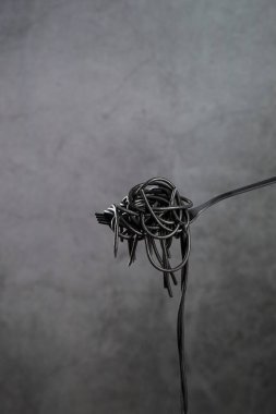 Sıcak siyah makarna, gri arkaplanda bir çatalla kopyalandı. Dikey biçim.