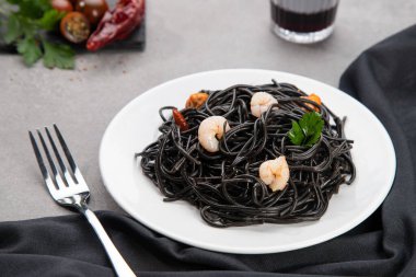 Beyaz tabakta mermer masa arkasında deniz mahsulleri olan siyah makarna. Seçici odak.