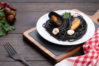 Ahşap zemin üzerinde deniz ürünleri olan bir tabak kara makarna. Akdeniz gıda kavramı.