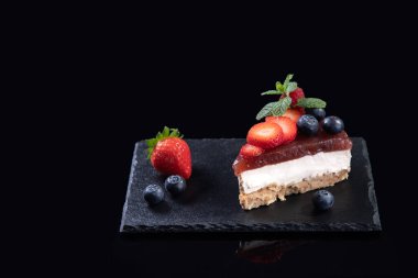 Taze çilek ve yaban mersinli cheesecake dilimi siyah arka planda, kopyalama alanı ile servis edilir. Ev yapımı fırın konsepti.