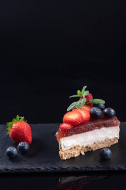 Cheesecake 'in bir parçası, siyah arkaplanda, kopyalama alanı ile birlikte servis edilen bir levhada izole edildi. Dikey format. Ev yapımı fırın konsepti.