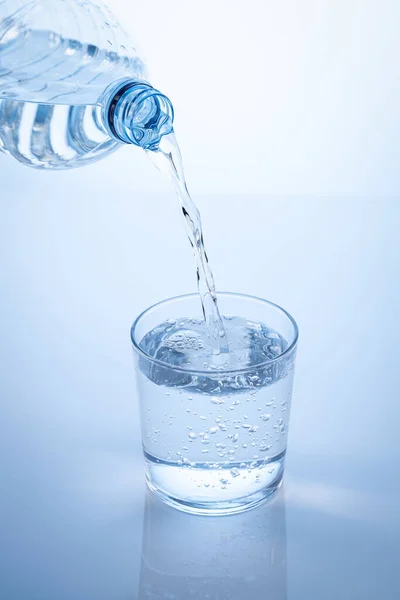 Pouring water from the bottle in to the glass isolated on blue background. Vertical format.