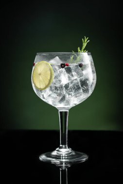 Cold glass of gin tonic with ice on dark green background with copy space. Vertical format.