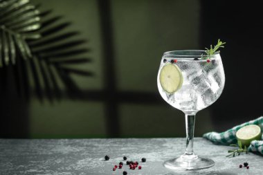 Gin tonic cocktail and shadows next to the window  on dark concrete background.