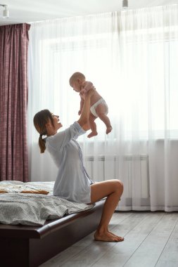 Yatakta neşeli bir anne, kucağında bebek