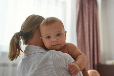 Kadının omzunda sevimli bir bebek, kameraya bakıyor.