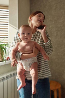 Annesinin kollarındaki sevimli bebek kameraya bakıyor.