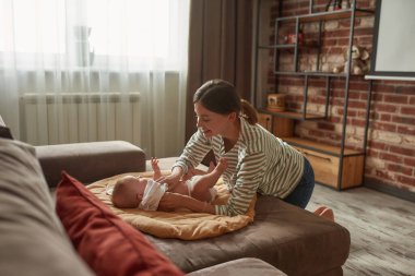 Bakıcı oturma odasındaki kanepede bebek kıyafetlerini değiştiriyor.