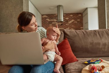 Endişeli anne çocuk doktoruna video araması sırasında bebek sıcaklığını kontrol ediyor.