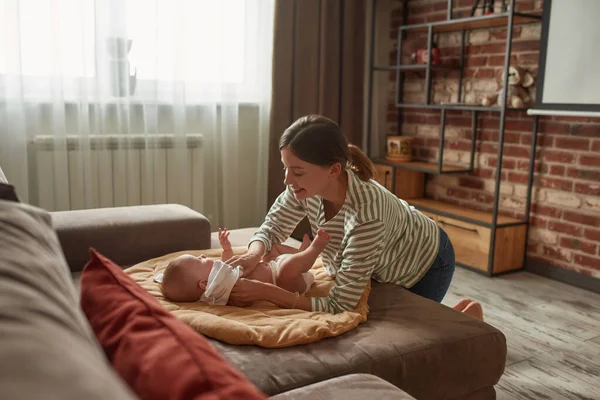 Bakıcı oturma odasındaki kanepede bebek kıyafetlerini değiştiriyor.