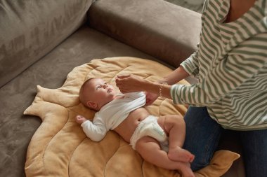 Annesinin kanepesinde düşünceli bir bebek gibi giyinmiş.