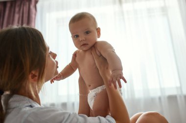 Annesinin meraklı küçük bebeği, pencerenin arka planında.