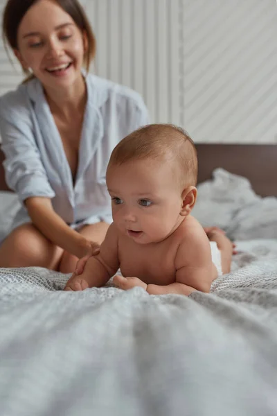 Young baby lying on tummy in bed near mother — Stock Photo, Image