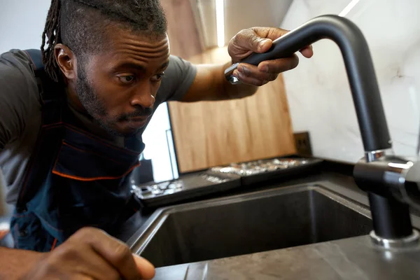 Closeup portrait African plumber holding kitchen tap