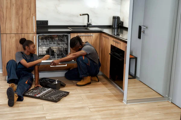 Männlicher Arbeiter repariert Waschmaschine, während Frau in der Nähe der Beleuchtung mit Taschenlampe sitzt — Stockfoto