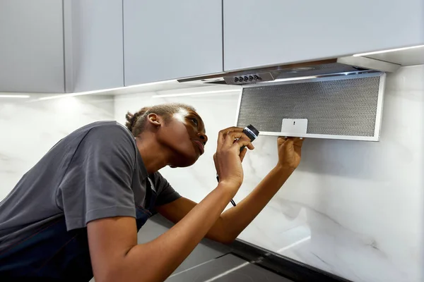 Kvinnlig arbetare reparera modern spis huva, hålla ficklampa i köket — Stockfoto