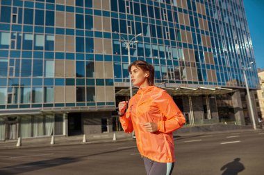 Kulaklıklı genç bir bayan dışarı koşuyor.