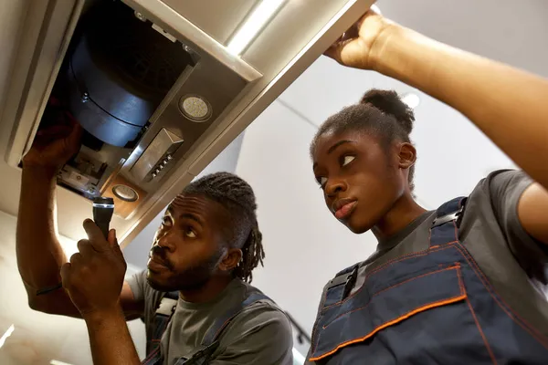 若い女性の見習いを説明する経験豊富な男性電気技師台所の排気問題を解決する方法 — ストック写真