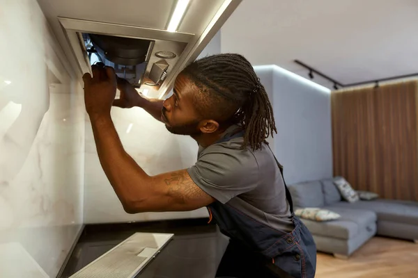 Closeup African American male electrician repairing kitchen extractor filter — Stock Photo, Image