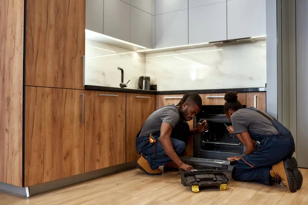 Dos reparadores afroamericanos frente al horno de cocina abierto — Foto de Stock