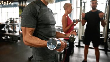Spor merkezinde ağır dambılları olan yaşlı bir vücut geliştirici.