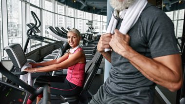 Tarz sahibi yaşlı bir kadın kapalı spor salonunda spor yapıyor.