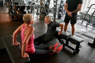 Orta yaşlı bir kadın spor salonunda erkek arkadaşıyla antrenman yapıyor.