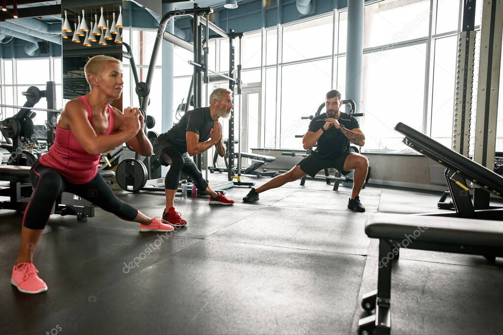 Mature woman and man doing side lunge exercise under trainers supervision