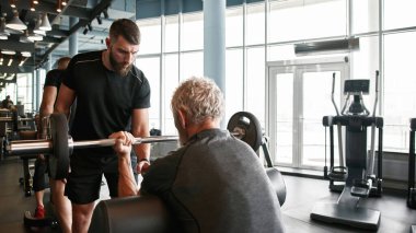 Profesyonel antrenör konsantre yüz ifadesi ile yardımcı kıdemli powerlifter