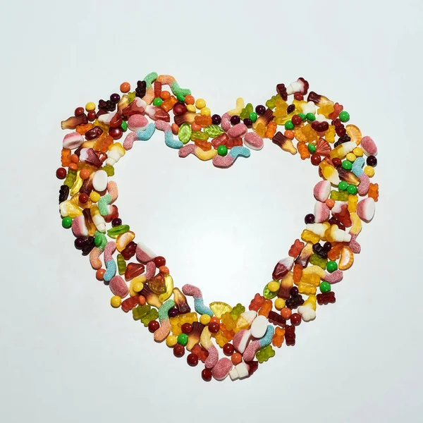 Renkli şekerlerin düzlüğü, beyaz arka planda izole edilmiş kalp şeklinde uzanan jöle şeker çeşitleri. — Stok fotoğraf
