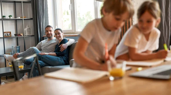 Lachend koppel ouders kijken naar kinderen die alleen studeren — Stockfoto