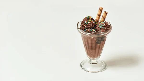 关闭了一勺美味的巧克力冰淇淋，上面撒满了甜谷粒和薄片棒，放在一个与浅色背景隔离的玻璃圣代菜里 — 图库照片
