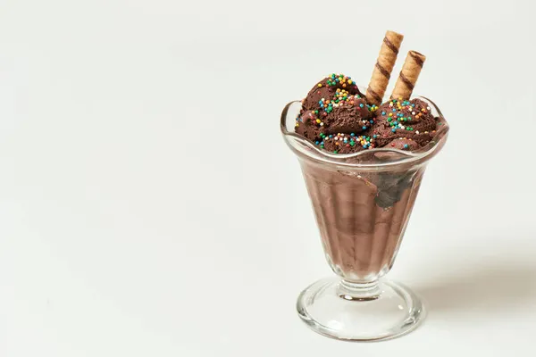 Скопления вкусного шоколадного мороженого, посыпанного сладким зерном и вафельными палочками в стеклянной тарелке с мороженым, изолированной на светлом фоне — стоковое фото