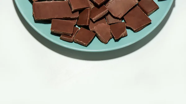 Ausgeschnittene Ansicht von zerkleinerten dunklen Schokoladentafeln stapeln sich auf einem Teller isoliert über weißem Hintergrund — Stockfoto