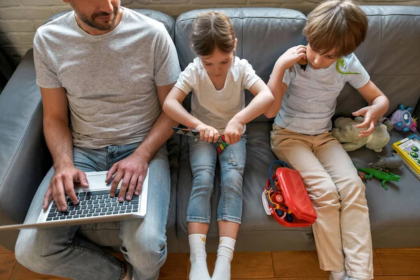Små barn spelar leksaker, pappa arbetar på laptop på nätet — Stockfoto