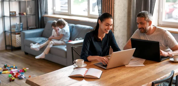 Sonriente pareja padres trabajan en línea en el ordenador portátil de la forma de casa —  Fotos de Stock