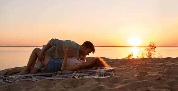 Passionate young couple kissing while lying together on the beach at sunset — Stock Photo, Image