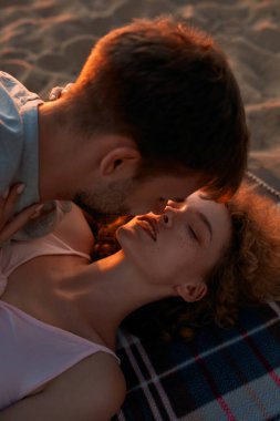 Gün batımında kumsalda birlikte vakit geçirirken aşık olan genç çift öpüşüyor.