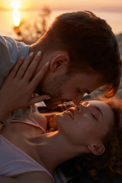 Retrato de jovem casal apaixonado beijando enquanto estavam deitados juntos na praia ao pôr do sol — Fotografia de Stock