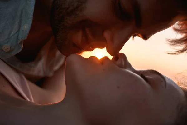 Fechar-se de jovem casal apaixonado beijando no pôr do sol enquanto relaxam juntos na praia — Fotografia de Stock