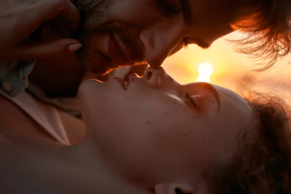 Fechar-se de homem jovem e mulher apaixonados beijando no pôr do sol enquanto relaxam juntos ao ar livre — Fotografia de Stock