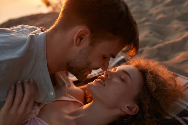 Двое влюбленных молодых людей обнимаются, лежа вместе на пляже на закате — стоковое фото