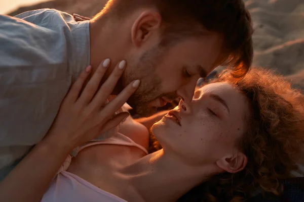 Portrait de deux jeunes amoureux s'embrassant alors qu'ils étaient couchés ensemble sur la plage au coucher du soleil — Photo