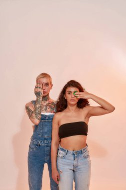 Yüzlerinin yarısını pembe arka planda izole edilmiş ellerle kaplayan farklı nesiller z lezbiyen çifti.