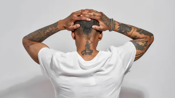 Visszapillantás tetovált fej, nyak és karok fiatal sötét bőrű férfi pózol elszigetelt fehér háttér — Stock Fotó